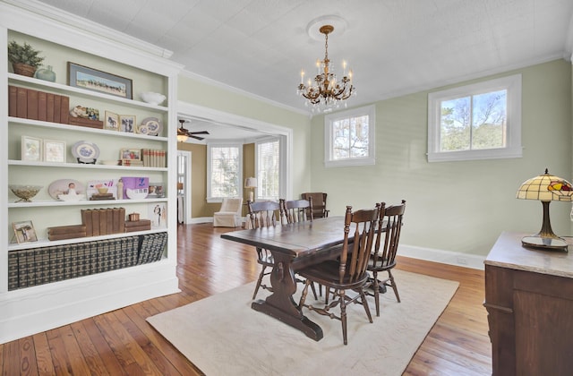 dining area featuring crown molding, built in shelves, ceiling fan with notable chandelier, and light hardwood / wood-style flooring