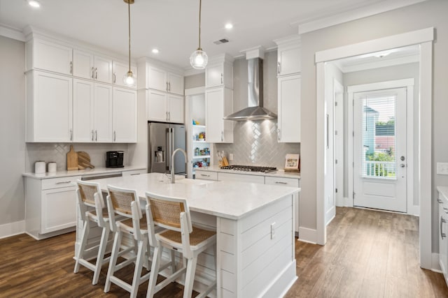 kitchen featuring white cabinets, appliances with stainless steel finishes, an island with sink, and wall chimney range hood