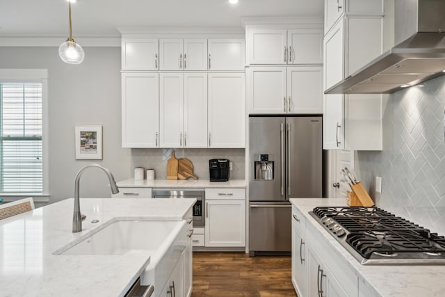 kitchen with pendant lighting, wall chimney exhaust hood, light stone countertops, white cabinetry, and stainless steel appliances