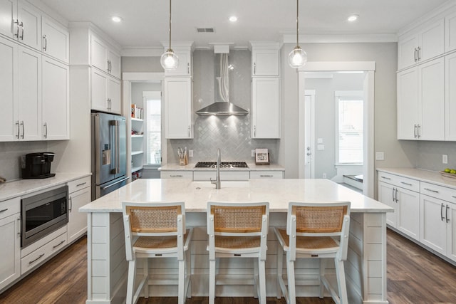 kitchen featuring white cabinets, an island with sink, wall chimney exhaust hood, and stainless steel appliances