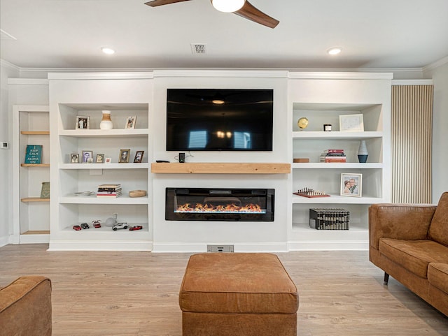 living room with a glass covered fireplace, wood finished floors, visible vents, and crown molding