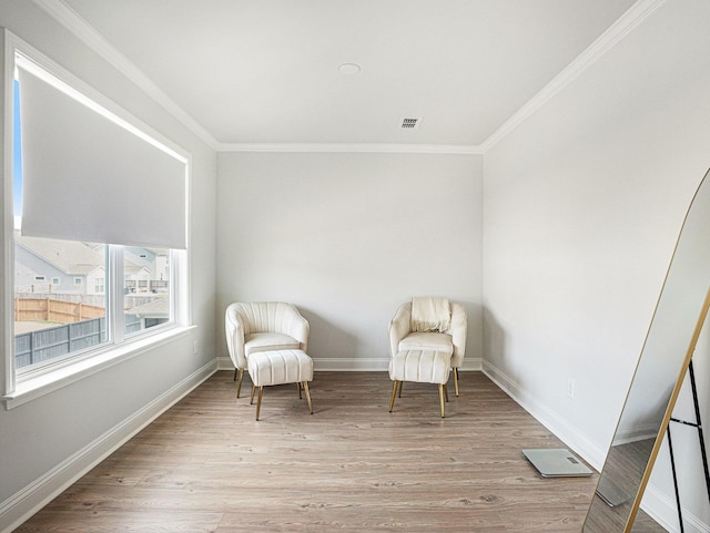 sitting room featuring baseboards, visible vents, light wood-style flooring, and crown molding