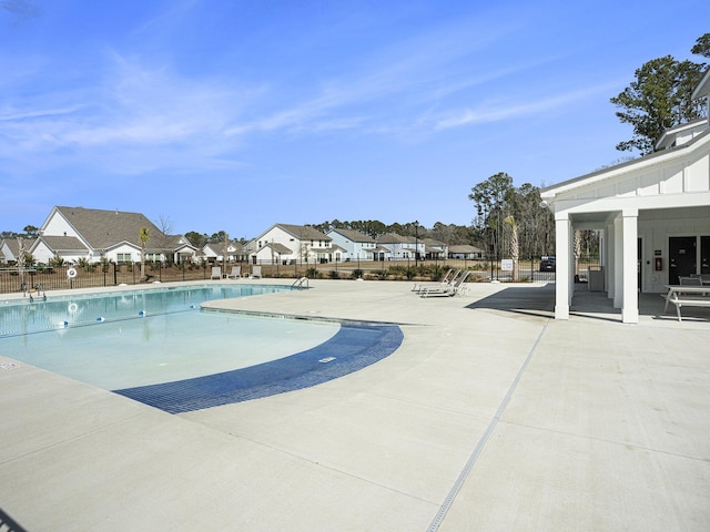 community pool with a patio, fence, and a residential view