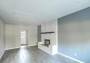 unfurnished living room with attic access, baseboards, wood finished floors, and a brick fireplace