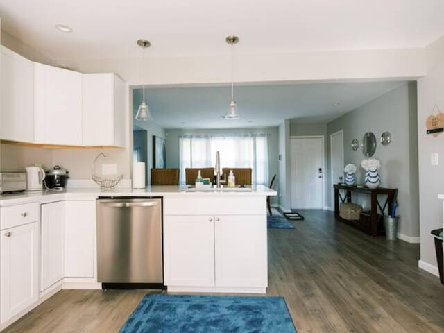 kitchen with stainless steel dishwasher, a sink, a peninsula, white cabinets, and light countertops