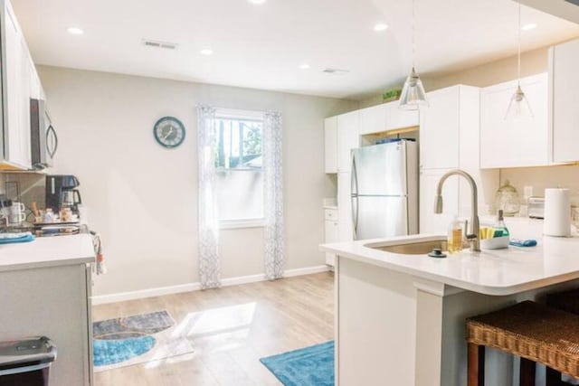 kitchen featuring freestanding refrigerator, a sink, light wood-type flooring, stainless steel microwave, and light countertops