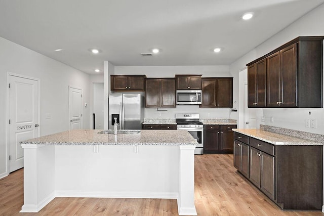 261 Celestial Blvd, Summerville, SC 29486 - kitchen with appliances with stainless steel finishes, light wood-style floors, dark brown cabinets, a kitchen island with sink, and light stone counters