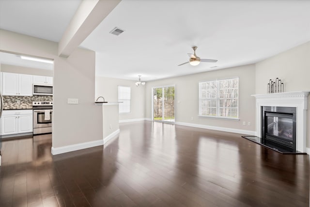 unfurnished living room with dark wood-style floors, visible vents, a glass covered fireplace, baseboards, and ceiling fan with notable chandelier