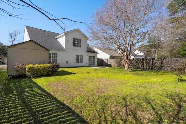 rear view of house featuring a patio, a shingled roof, a lawn, and fence