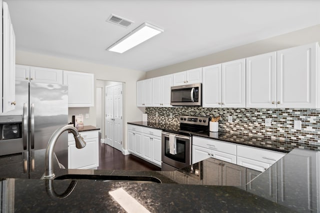 kitchen with tasteful backsplash, visible vents, white cabinets, stainless steel appliances, and a sink