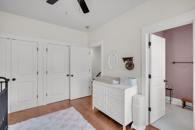 bedroom with light wood-type flooring, ceiling fan, and two closets