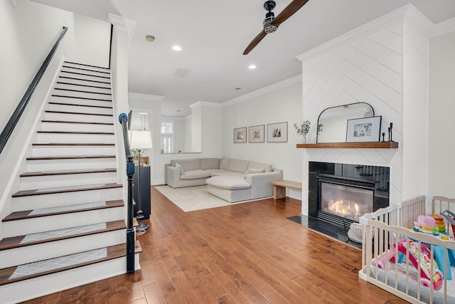 living room featuring hardwood / wood-style flooring, ceiling fan, a large fireplace, and crown molding