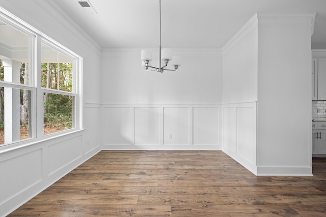 unfurnished dining area with dark hardwood / wood-style floors, crown molding, and a chandelier