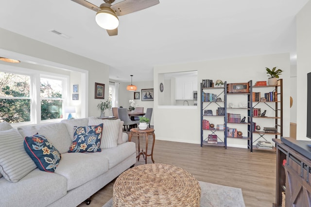 living area with baseboards, wood finished floors, visible vents, and ceiling fan