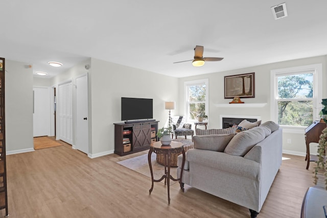 living area featuring visible vents, light wood-style flooring, a fireplace, and baseboards