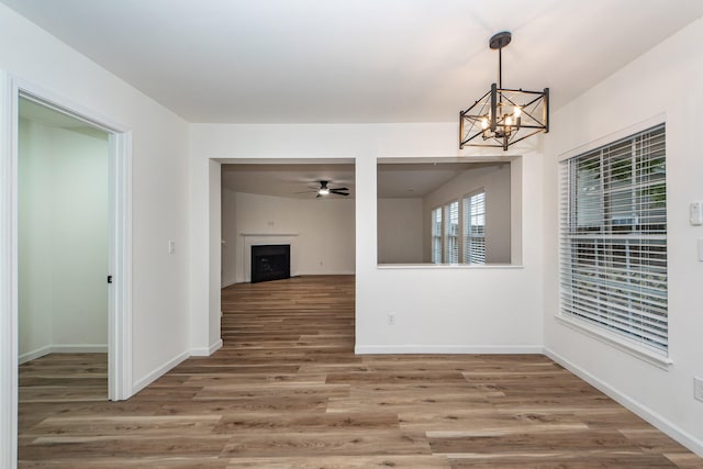 unfurnished dining area with ceiling fan with notable chandelier and hardwood / wood-style flooring