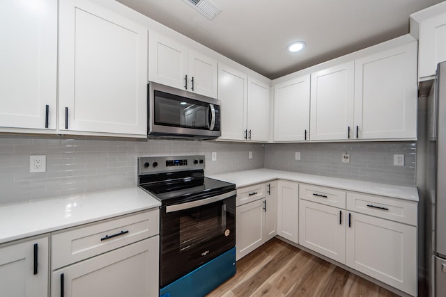 kitchen featuring white cabinets, appliances with stainless steel finishes, hardwood / wood-style flooring, and decorative backsplash