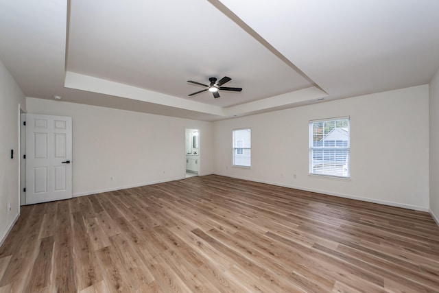 empty room featuring a raised ceiling, light hardwood / wood-style flooring, and ceiling fan