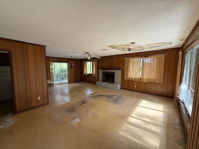 unfurnished living room with a textured ceiling, a brick fireplace, ceiling fan, and wood walls