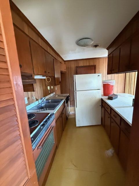 kitchen featuring wood walls, sink, white fridge, and stainless steel range with electric cooktop