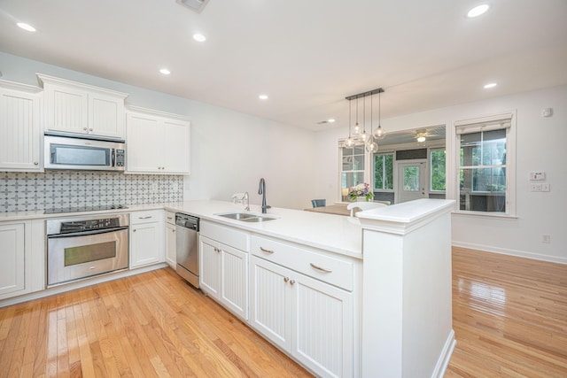 kitchen featuring pendant lighting, light hardwood / wood-style flooring, appliances with stainless steel finishes, kitchen peninsula, and sink