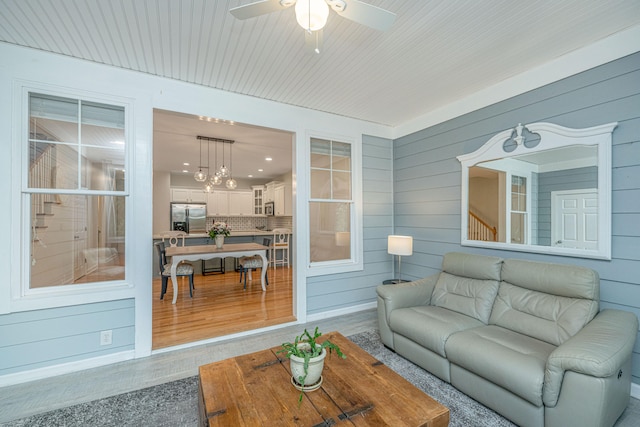 living room with ceiling fan with notable chandelier, wood-type flooring, and wooden walls