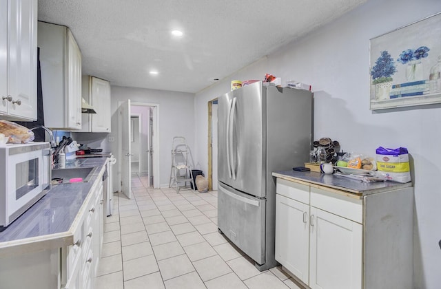 7074 W Constellation Dr, North Charleston, SC 29418 - kitchen with freestanding refrigerator, light tile patterned flooring, white cabinetry, under cabinet range hood, and a textured ceiling