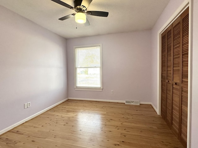 unfurnished bedroom with ceiling fan, a textured ceiling, a closet, and light wood-type flooring