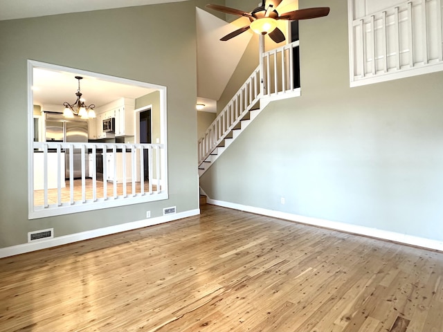 interior space featuring ceiling fan with notable chandelier, high vaulted ceiling, and light hardwood / wood-style flooring