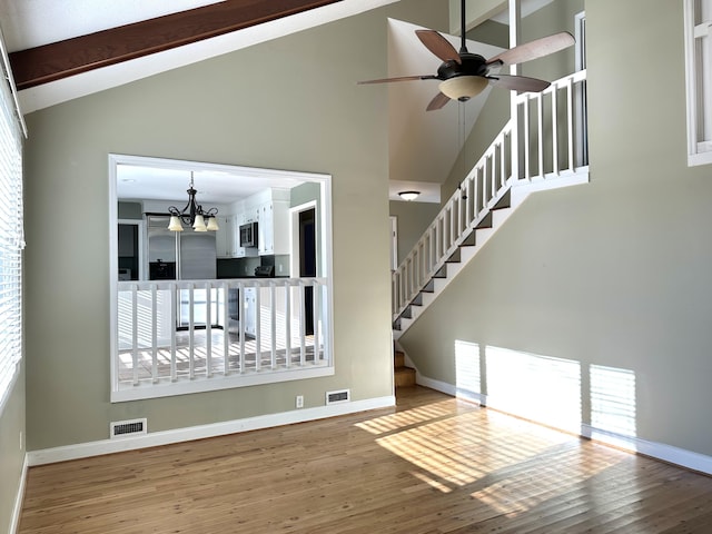 unfurnished living room featuring hardwood / wood-style flooring, ceiling fan with notable chandelier, high vaulted ceiling, and beamed ceiling