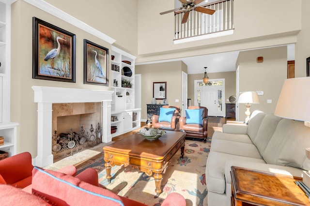 living room with a tile fireplace, a towering ceiling, built in features, and ceiling fan