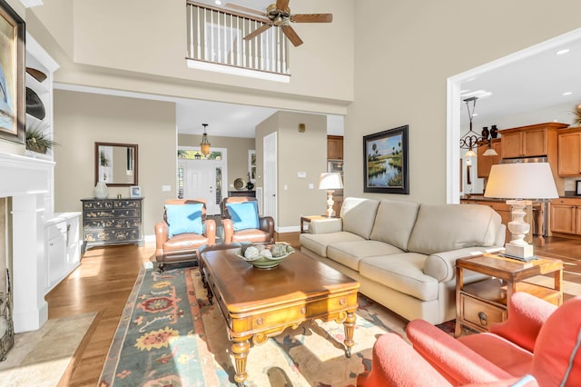 living room with a high ceiling, a premium fireplace, ceiling fan, and light wood-type flooring