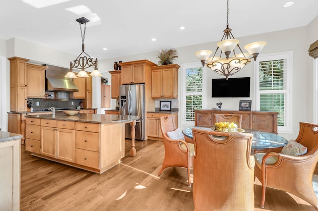 kitchen with ventilation hood, decorative light fixtures, a center island with sink, and stainless steel fridge with ice dispenser