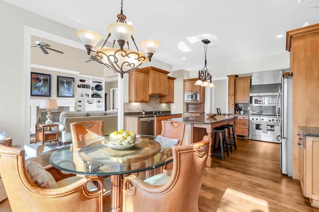 dining space with ceiling fan with notable chandelier, sink, and light wood-type flooring