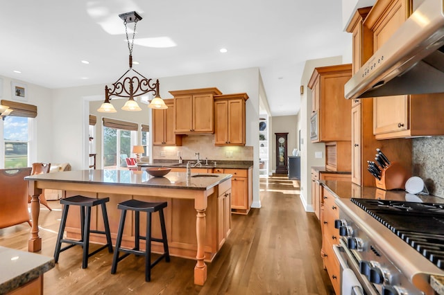 kitchen featuring pendant lighting, dark stone countertops, a center island with sink, stainless steel appliances, and a kitchen bar