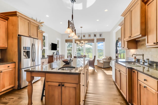 kitchen with stainless steel refrigerator with ice dispenser, sink, hanging light fixtures, dark stone countertops, and a kitchen island with sink