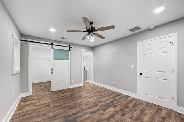 unfurnished bedroom featuring a barn door, a closet, ceiling fan, and dark wood-type flooring