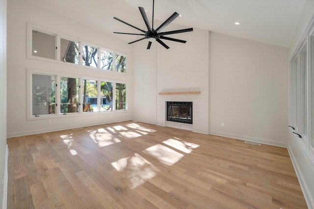 unfurnished living room with ceiling fan, a large fireplace, a high ceiling, and light hardwood / wood-style flooring