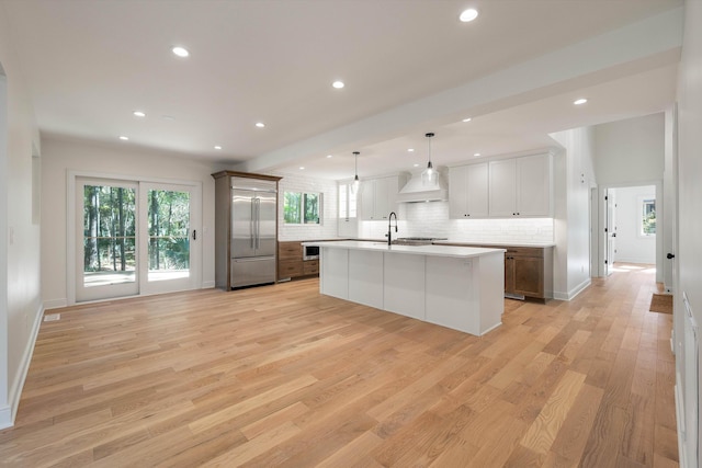 kitchen featuring a center island with sink, decorative light fixtures, built in fridge, and light hardwood / wood-style flooring