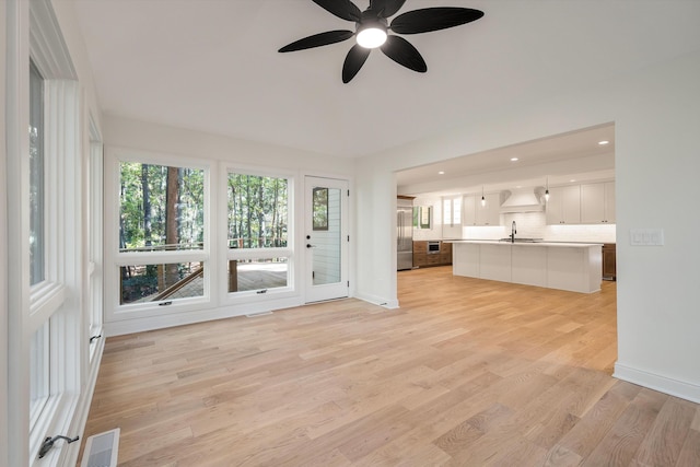 unfurnished living room featuring ceiling fan, sink, and light hardwood / wood-style flooring