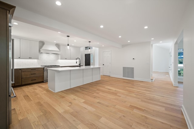 kitchen with a center island with sink, light hardwood / wood-style floors, high end stainless steel range oven, and custom exhaust hood