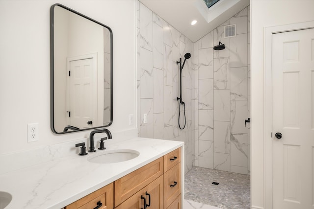 bathroom with lofted ceiling with skylight, vanity, and tiled shower