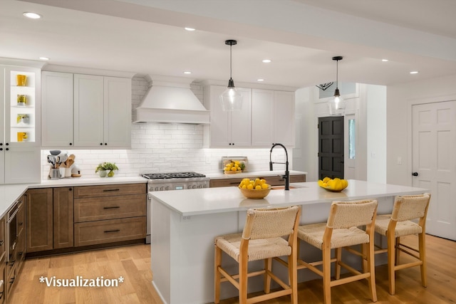 kitchen featuring premium range hood, light hardwood / wood-style flooring, white cabinetry, and a center island with sink