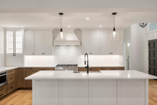 kitchen featuring white cabinets, light hardwood / wood-style floors, custom range hood, and a kitchen island with sink