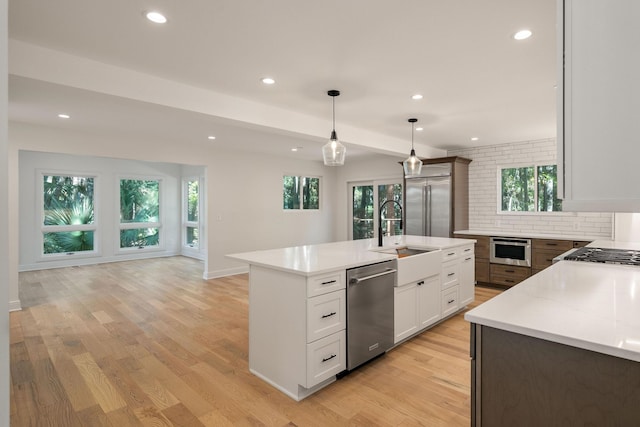 kitchen featuring an island with sink, light hardwood / wood-style floors, decorative light fixtures, white cabinets, and appliances with stainless steel finishes