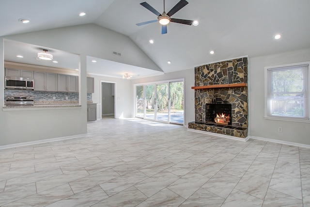 unfurnished living room with ceiling fan, a stone fireplace, plenty of natural light, and high vaulted ceiling