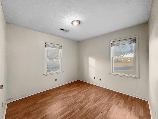 empty room featuring visible vents, a textured ceiling, baseboards, and wood finished floors