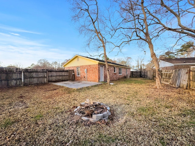 exterior space with a fire pit, a fenced backyard, a yard, a patio area, and brick siding