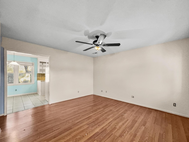 unfurnished room with wood finished floors, a ceiling fan, and baseboards