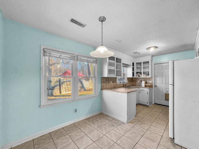 kitchen with visible vents, backsplash, freestanding refrigerator, white cabinetry, and a peninsula